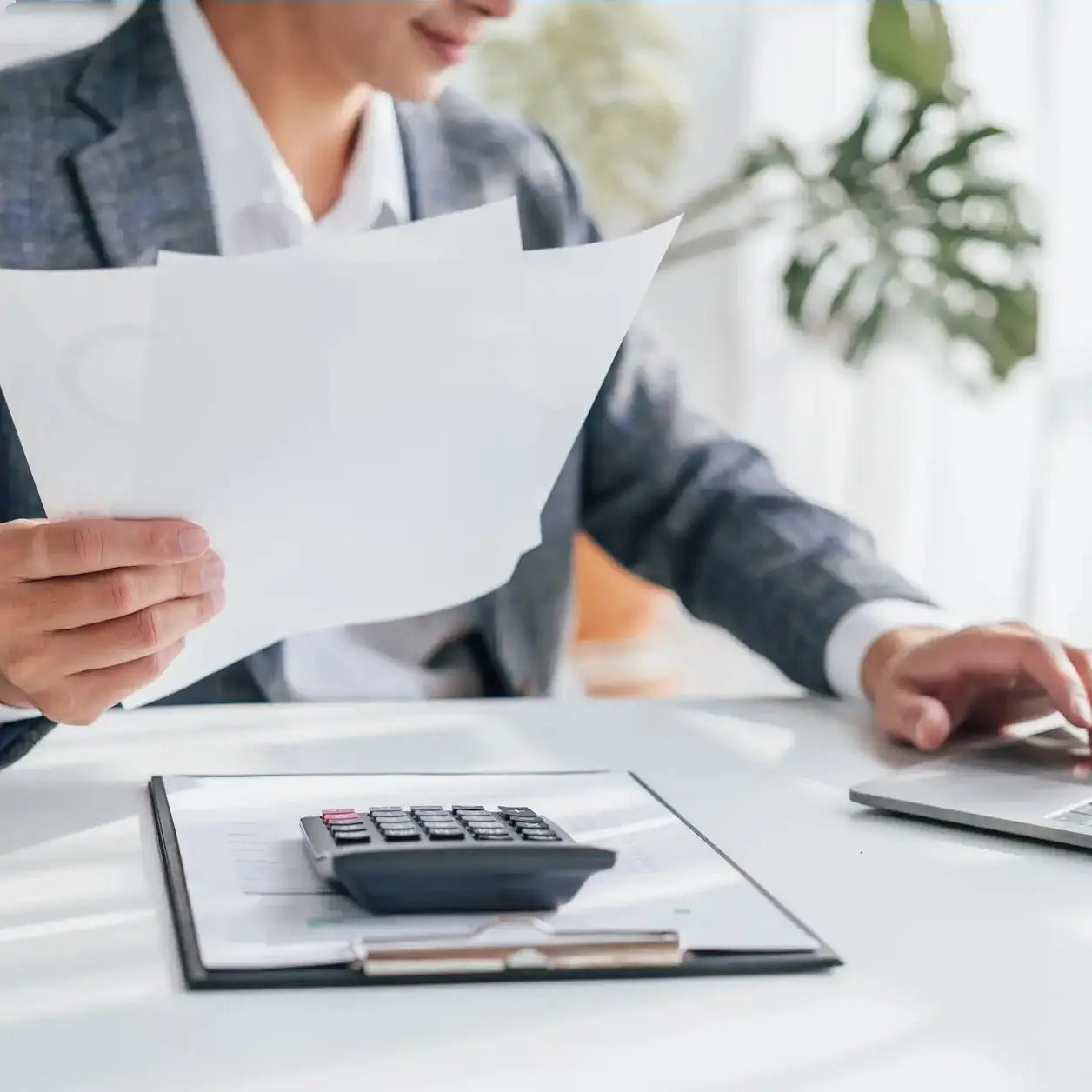 Accountant reviewing paperwork at a desk with a calculator and laptop